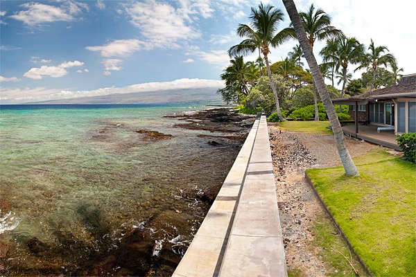View of railing, with lawn and palm trees on one side and shallow  ocean on the other