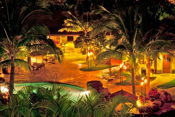 pool with palm trees illuminated by tiki torches at night